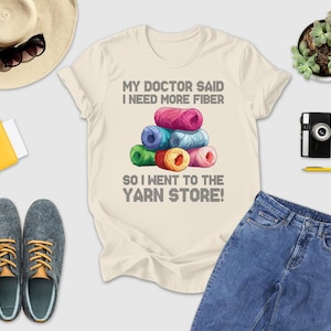 a casual outfit laid out on a white background, including a t-shirt with a humorous text, a hat, sunglasses, a camera, a wallet, a pair of shoes, and a potted plant.