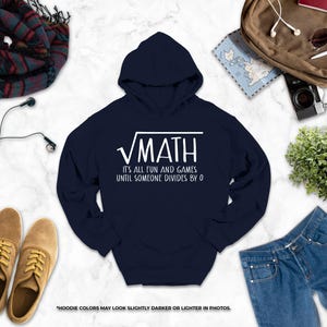 a navy blue hoodie with a white text design, a pair of brown shoes, a pair of blue jeans, a camera, a map, a scarf, and a plant, all arranged on a white marble surface.