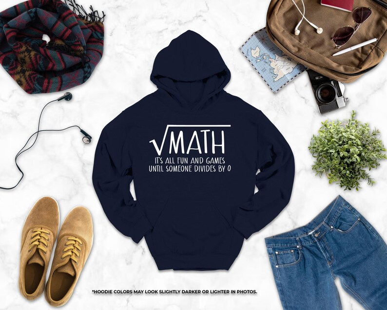 a navy blue hoodie with a white text design, a pair of brown shoes, a pair of blue jeans, a camera, a map, a scarf, and a plant, all arranged on a white marble surface.