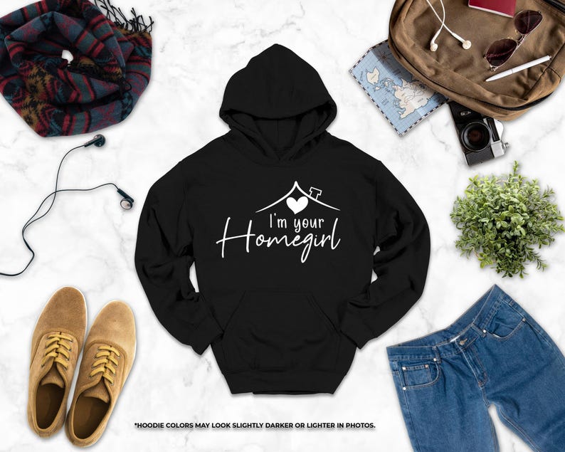 a variety of clothing and accessories, including a black hoodie with the text "I'm your Homegirl" printed on it, a pair of brown shoes, a pair of blue jeans, a scarf, a camera, and a plant.