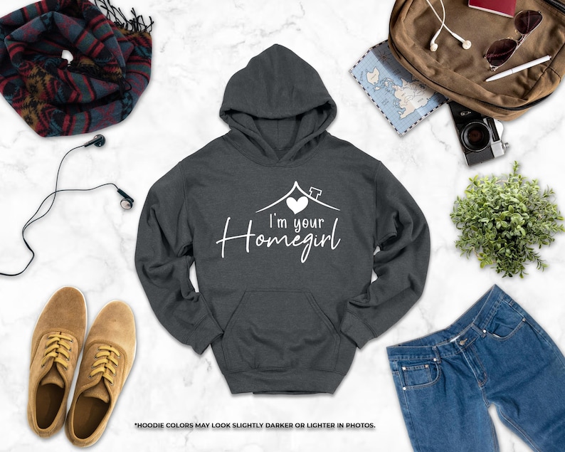 a casual outfit consisting of a gray hoodie with the text "I'm your Homegirl" printed on it, along with a pair of jeans, a pair of brown shoes, and a backpack. The items are arranged on a marble surface, creating a visually appealing and organized display.