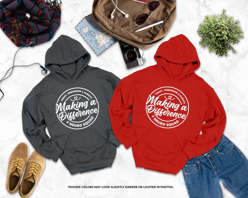 two hooded sweatshirts with the same design, one gray and one red, laid out on a marble surface along with various other items such as a camera, a plant, and a pair of shoes.