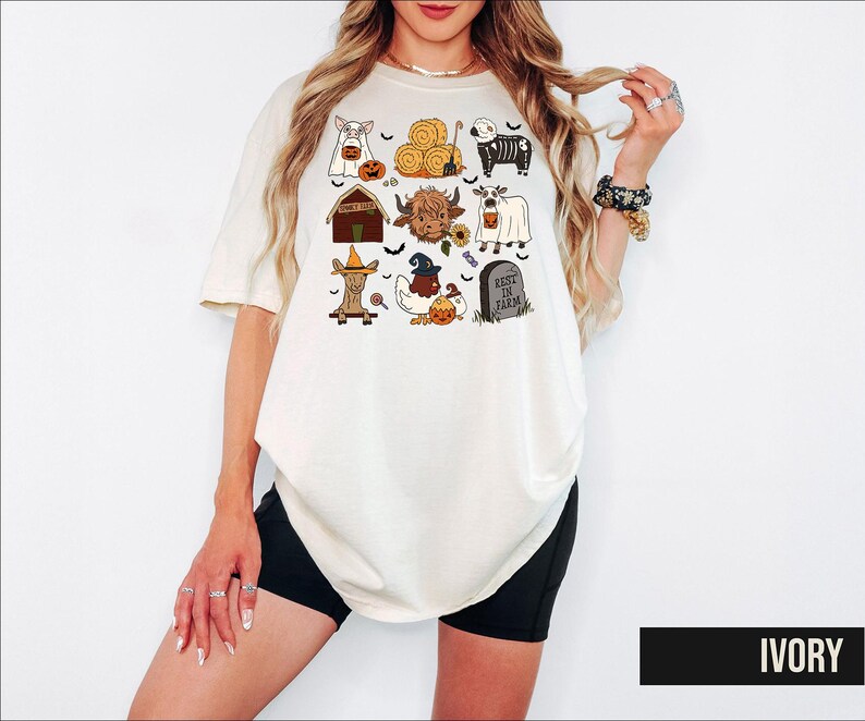 A woman wearing a white t-shirt with a graphic design of various Halloween-themed items, including a skeleton, a pumpkin, a ghost, and a barn.