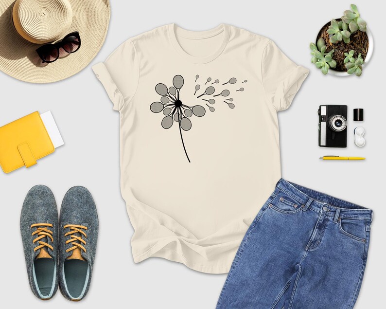 a casual outfit consisting of a white t-shirt with a graphic design, a pair of blue jeans, gray shoes, a straw hat, sunglasses, a yellow wallet, a camera, a pen, and a potted plant.