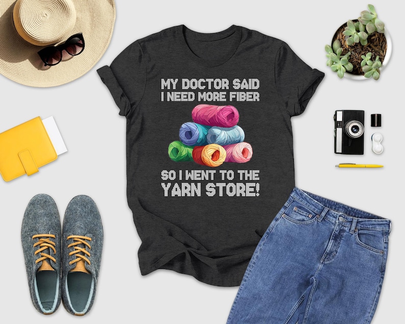 a black t-shirt with a humorous text, a stack of colorful yarn, a hat, sunglasses, a camera, a wallet, a pair of shoes, and a potted plant.