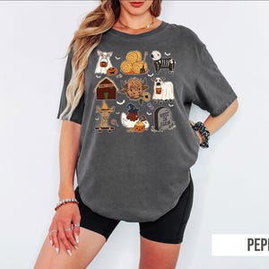 A woman wearing a gray t-shirt with a graphic design of various Halloween-themed illustrations, including pumpkins, bats, and other spooky elements.