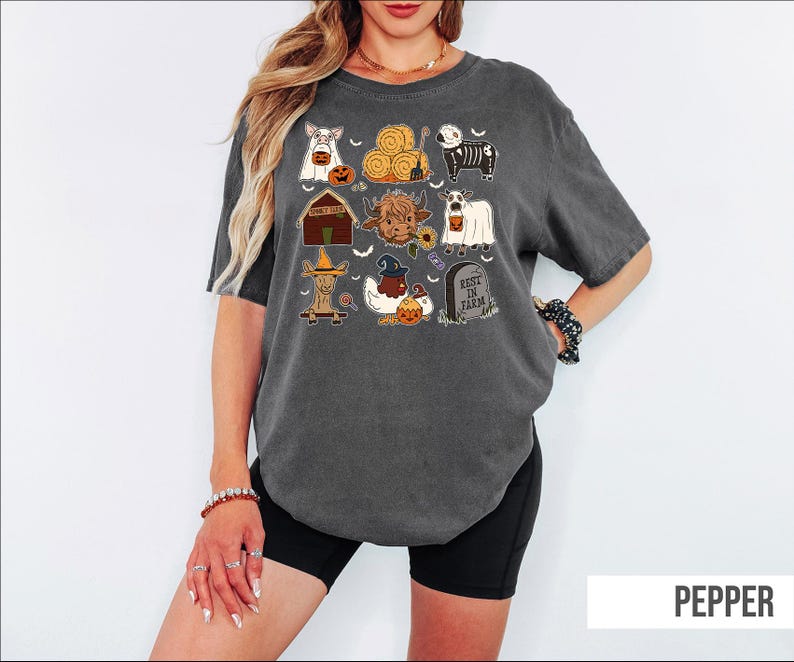 A woman wearing a gray t-shirt with a graphic design of various Halloween-themed illustrations, including pumpkins, bats, and other spooky elements.