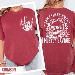 a red t-shirt with a graphic design on the back, including a skull and floral elements, along with the text "Sometimes Sweet Mostly Savage".