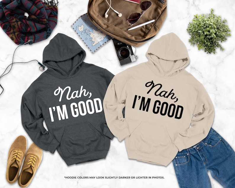 two hooded sweatshirts with the text "Nah, I'm good" printed on them, along with a pair of jeans and some accessories such as a backpack, sunglasses, and a plant.