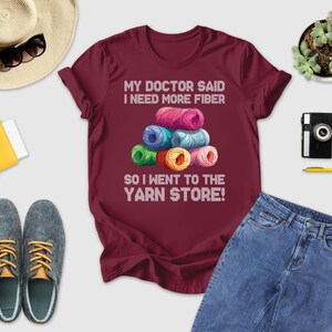 a variety of items, including a maroon t-shirt with a humorous text, a hat, sunglasses, a camera, a book, a plant, and a pair of shoes.