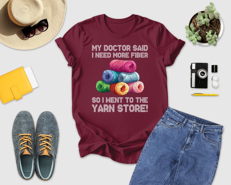 a variety of items, including a maroon t-shirt with a humorous text, a hat, sunglasses, a camera, a book, a plant, and a pair of shoes.