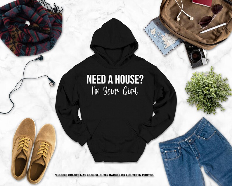 a black hoodie with the text "NEED A HOUSE? I'M YOUR GIRL" printed on it, along with various clothing items such as jeans, a pair of shoes, and a backpack.