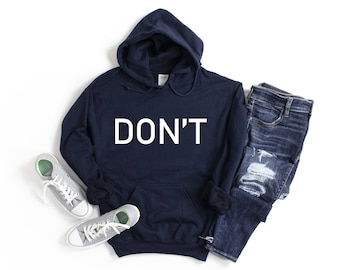 Peut inclure: Un sweat à capuche bleu marine avec le mot "DON'T" en lettres blanches. L'image présente également un jean bleu délavé et des baskets grises avec des lacets blancs.