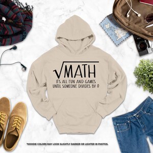 a casual outfit laid out on a marble surface, including a hoodie with a humorous math-themed design, a pair of brown shoes, a pair of blue jeans, a scarf, a camera, and a plant.