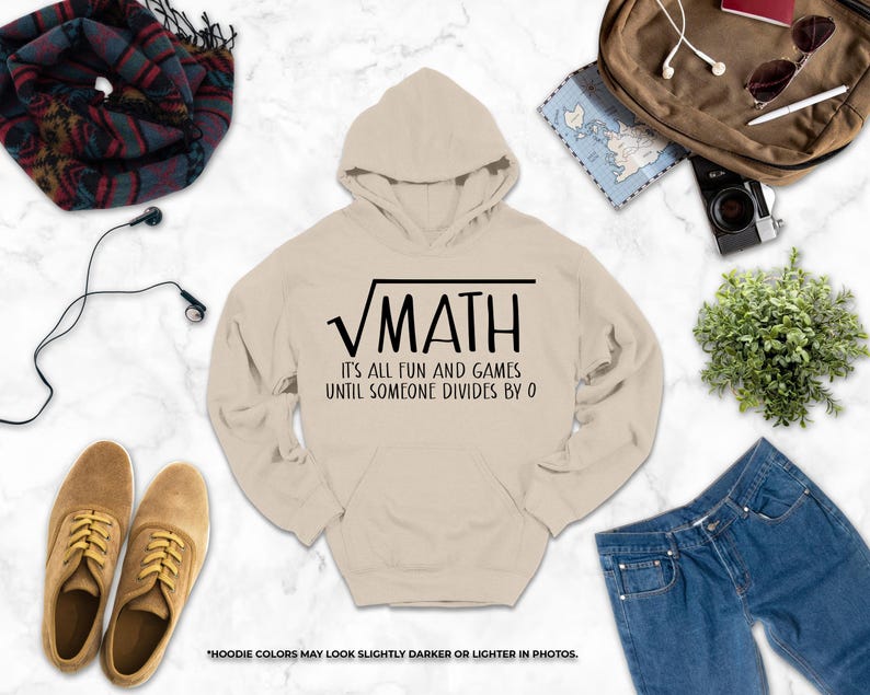 a casual outfit laid out on a marble surface, including a hoodie with a humorous math-themed design, a pair of brown shoes, a pair of blue jeans, a scarf, a camera, and a plant.