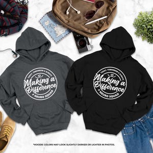 two hooded sweatshirts with the same design, laid out on a marble surface alongside other items such as a backpack, a pair of jeans, and a pair of shoes.