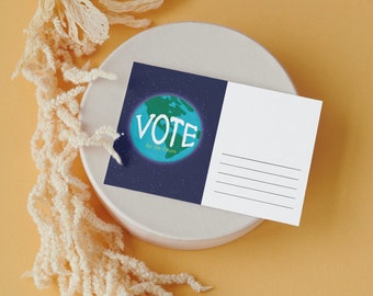 Puede incluir: Una postal con un fondo azul y un globo terráqueo verde y blanco que dice "VOTE for the future". La postal está sobre un plato circular blanco con un fondo amarillo. Una planta beige seca está en el lado izquierdo de la imagen.