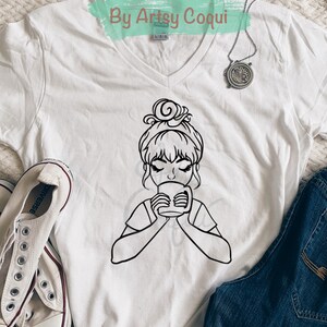 以下が含まれることがあります： 白いTシャツに、髪の毛をまとめた女性がマグカップから飲んでいる黒い線画が描かれています。Tシャツの上部には「Digital Download By Artsy Coqui」というテキストがあります。
