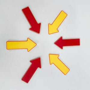 May include: Arrangement of six arrows, three red and three yellow, pointing towards a central point. The arrows have a glossy finish and are set against a white background. The arrows are a simple, graphic design.
