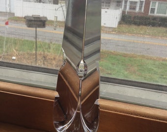 May include: A clear glass decorative object shaped like a feather with a wide base. The object is sitting on a wooden surface.