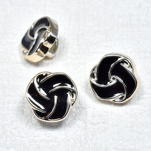 Op de afbeelding: Drie ronde, decoratieve knopen in zwart en goud met een knoopontwerp. De knopen hebben een glanzende afwerking.