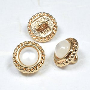 May include: Three gold-toned buttons with a rope-like design around the edge. Two buttons have a white pearl-like center, and one button has a gold-toned center with the text "F.S.K. 10M" engraved on it.