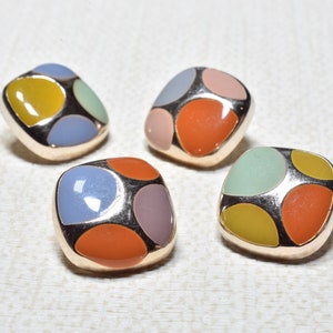 Op de afbeelding: Vier vierkante knopen met een gouden metalen frame en kleurrijke emaille accenten. Elke knop heeft vier verschillende gekleurde cirkels in het midden. De kleuren zijn geel, oranje, blauw, groen en roze.