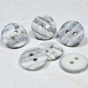 以下が含まれることがあります： 2つの穴が空いた白とグレーの大理石模様の丸いボタンが6つあります。ボタンは滑らかな表面をしています。