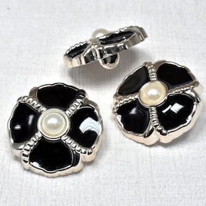 Könnte beinhalten: Drei schwarze und silberne, blumenförmige Knöpfe mit einer weißen Perle in der Mitte jedes Knopfes.