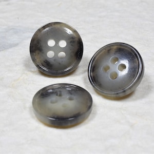 May include: Three round, four-hole buttons with a mottled gray and white pattern.