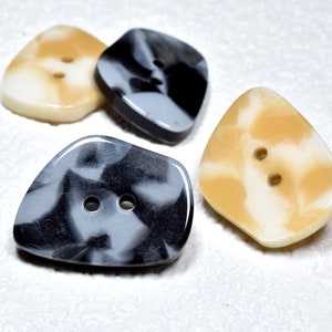 Puede incluir: Cuatro botones de dos agujeros en una variedad de colores y patrones. Dos botones son blancos con remolinos marrones, y dos botones son negros y blancos con remolinos.