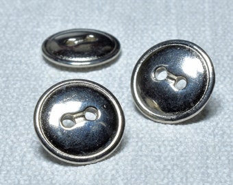Op de afbeelding: Drie zilveren metalen knopen met elk twee gaten. De knopen zijn rond en hebben een glanzende afwerking.