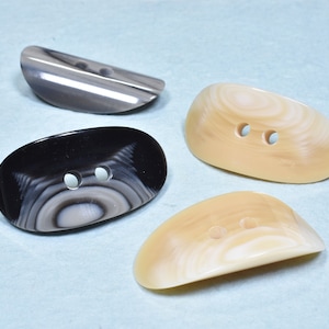 May include: Four shell buttons with two holes each. The buttons are in various shades of brown and black with a swirling pattern.