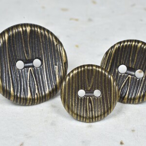 May include: Three round, two-hole buttons with a woodgrain pattern. The buttons are made of metal and have a gold and brown finish.