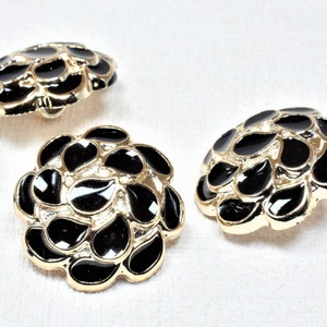 May include: Three black and gold buttons with a floral design. Each button has a raised design of black teardrop shapes on a gold background.