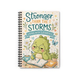 以下が含まれることがあります： 「Stronger Than The Storms, Living With Sjogren's」の文字が入ったスパイラルノート。表紙には、メガネをかけた漫画の恐竜がノートに書き込み、コーヒーカップ、花、蝶が描かれています。
