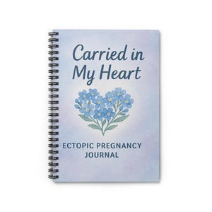 May include: A spiral-bound journal with a soft, watercolor-style cover. The cover features the text "Carried in My Heart" in dark blue script above a heart-shaped arrangement of blue flowers. Below the flowers, the text reads "Ectopic Pregnancy Journal."