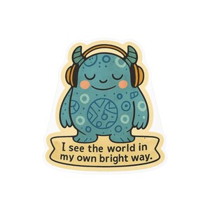 May include: A die-cut sticker featuring a teal monster with circular patterns, wearing orange headphones. The monster has closed eyes and pink cheeks. Below the monster, a cream-colored banner displays the text: I see the world in my own bright way.