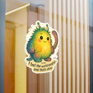 May include: A colorful sticker featuring a cute, cartoonish monster with a yellow body, green spiky hair, and a purple arm. The sticker has the text "I feel the world deeply - and that's okay."