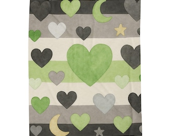 Puede incluir: Una manta con un patrón repetido de corazones, lunas y estrellas en tonos verdes, grises y negros sobre un fondo a rayas. La manta tiene un aspecto suave y texturizado, adecuada para la decoración del hogar.