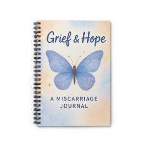 May include: Spiral-bound journal with the words "Grief & Hope" and "A Miscarriage Journal" on the cover. A blue butterfly is centered on a watercolour background of blue, peach, and yellow. Gold stars are scattered around the butterfly.