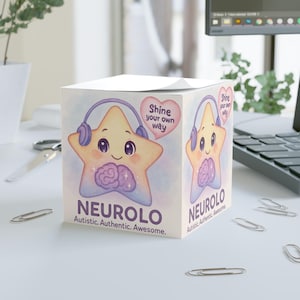 Puede incluir: Un bloc de notas cúbico con un personaje de estrella de dibujos animados con auriculares y un gráfico de cerebro. Se muestra el texto "NEUROLO" y "Autistic. Authentic. Awesome.". Un corazón dice "Shine your own way."