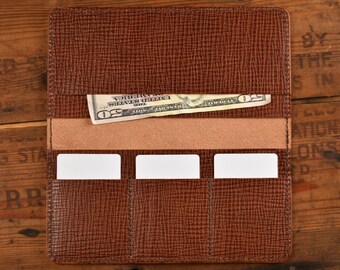 May include: A brown leather wallet with three card slots and a billfold. A twenty dollar bill is visible in the billfold.