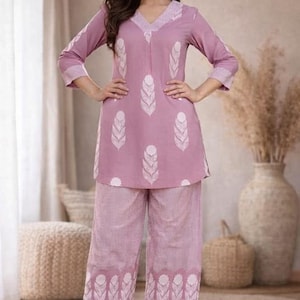May include: Mauve two-piece pyjama set with a tunic top and wide-leg trousers. The top has a V-neck and white feather-like designs. The trousers have a matching pattern. The set is made of a soft fabric. The brand logo "SIYABUN" is visible.