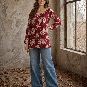 May include: A burgundy floral top with a square neckline and long sleeves, worn with light blue wide-leg jeans. The image is set in a room with a window and a logo in the top right corner.