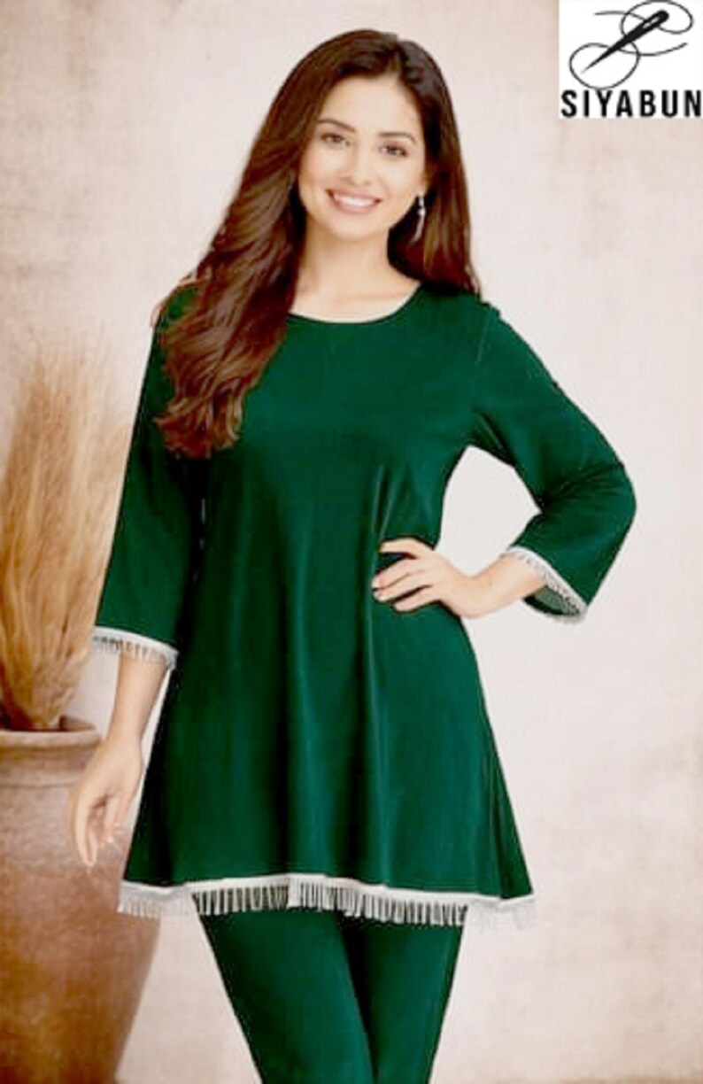 May include: A dark green tunic and leggings set with white lace trim. The tunic has three-quarter sleeves and a rounded neckline. The logo "SIYABUN" is in the upper right corner. The model is smiling.