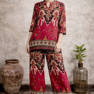 May include: A two-piece outfit featuring a red top and wide-leg pants with a floral pattern in black, brown, and green. The top has a V-neck and three-quarter sleeves. The outfit is from the brand SIYABUN.