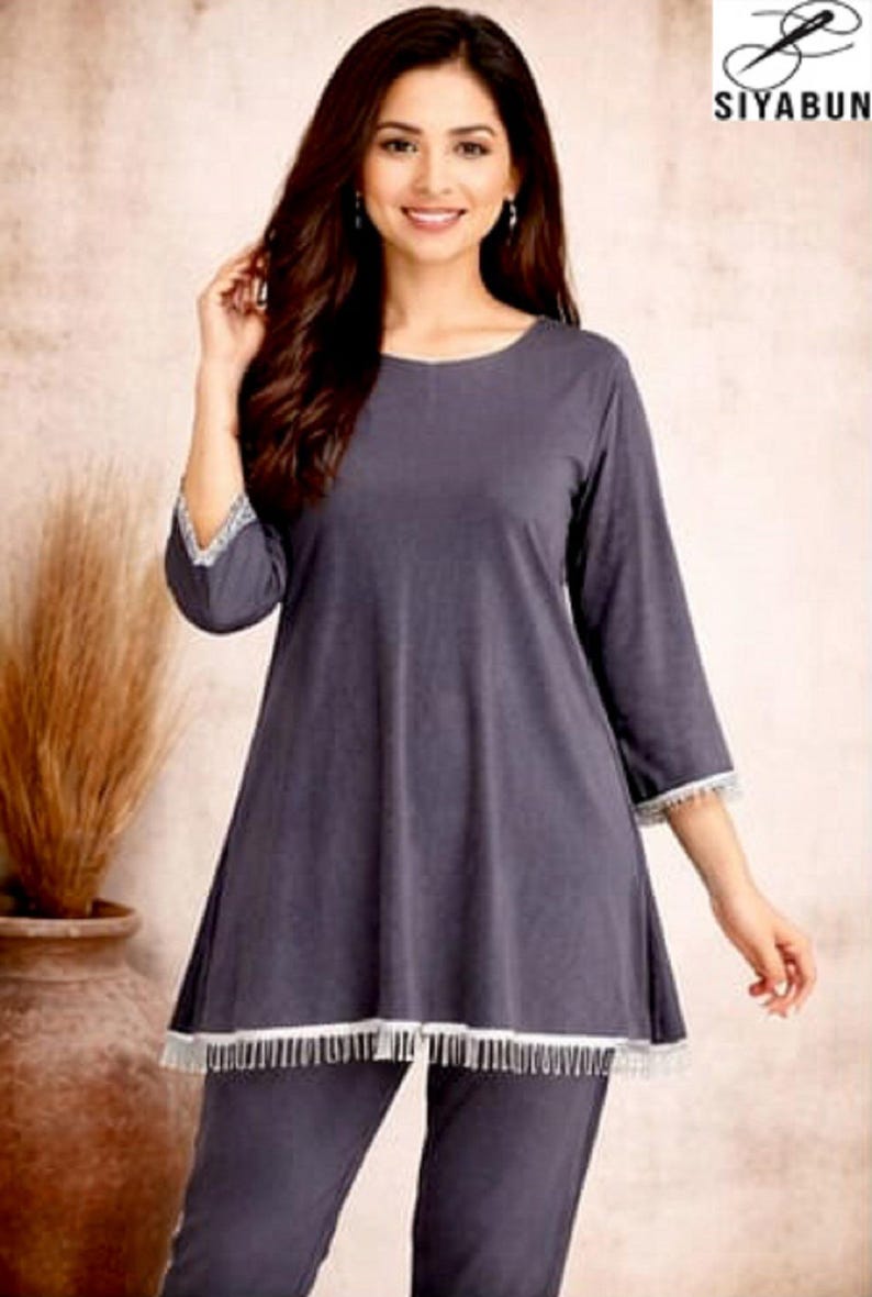 May include: A dark gray pajama set with a tunic-style top and matching pants. The top has three-quarter sleeves and a white fringe trim at the hem and sleeve cuffs. The image includes the brand logo "SIYABUN".