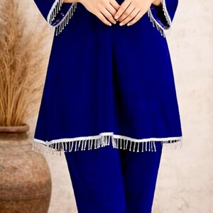 May include: A royal blue two-piece outfit. The top has long sleeves and a flared hem, both trimmed with white fringe. The matching pants complete the ensemble. The logo "SIYABUN" is visible in the upper right corner.