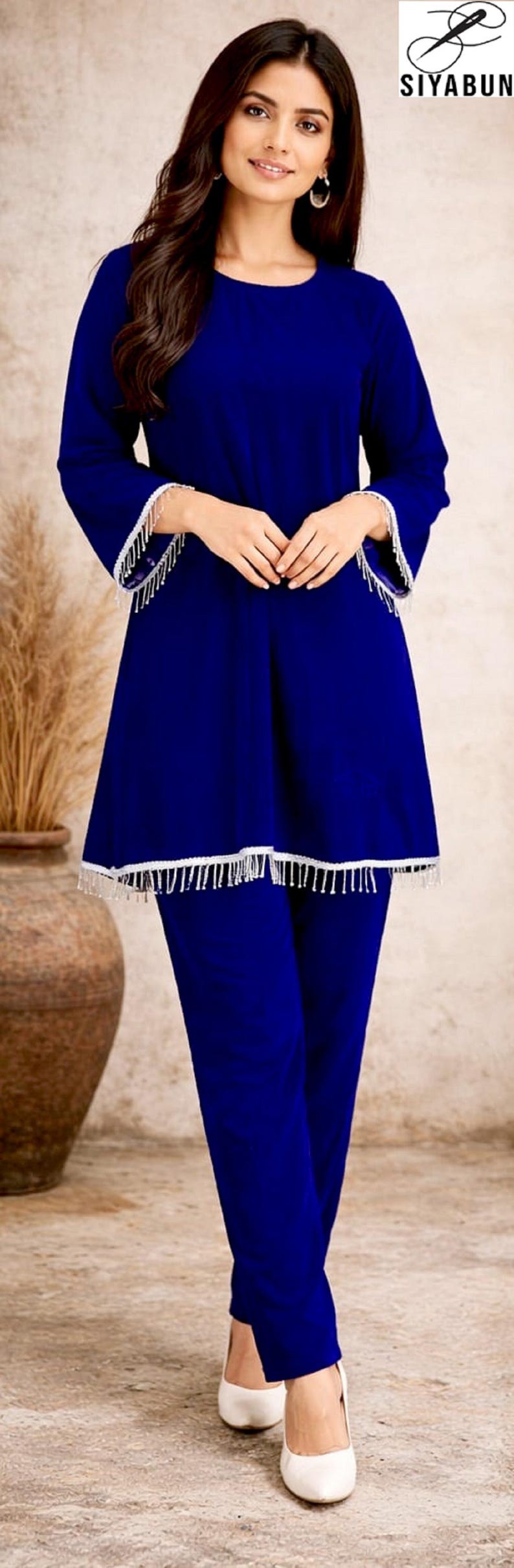 May include: A royal blue two-piece outfit. The top has long sleeves and a flared hem, both trimmed with white fringe. The matching pants complete the ensemble. The logo "SIYABUN" is visible in the upper right corner.